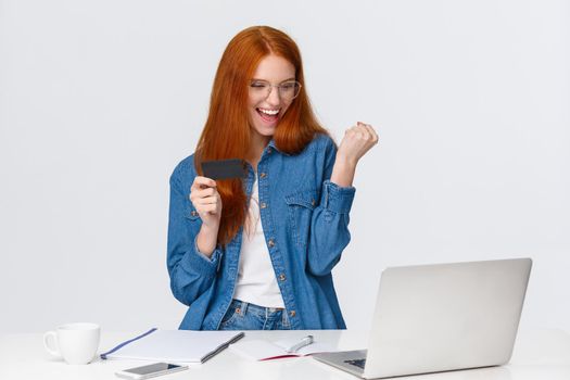 Satisfied, excited and triumphing good-looking redhead girl fist pump, bought thing with good discount, say yes celebrating, shopping online, holding credit card, won bonuses, white background
