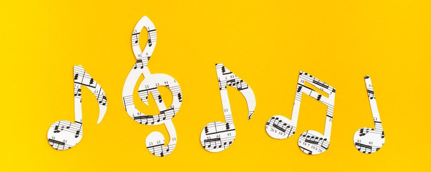Musical notes and clef cut from paper with musical text in a row on yellow background. Web banner