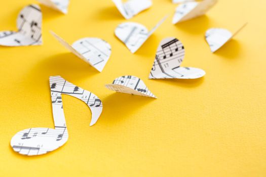 Musical notes, clef and hearts cut from paper with musical text on yellow background