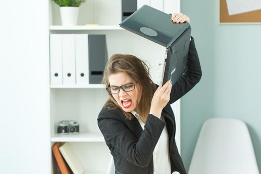 Stress, office and people concept - stressed angry business woman breaking up her computer