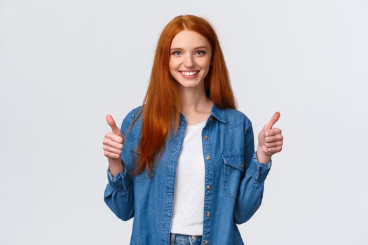 Waist-up portrait alluring confident smiling redhead female blogger review awesome new product, showing thumbs-up in approval, like or agree gesture, standing white background
