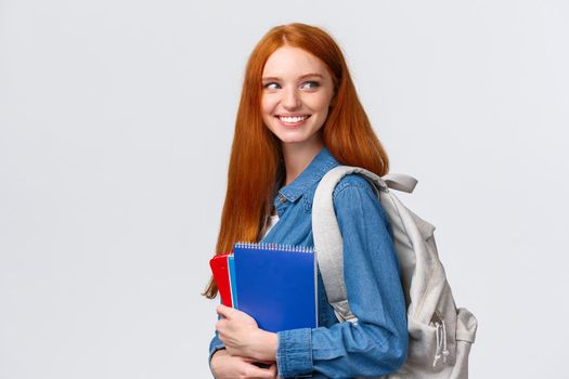 Girl seeing classmate in hall saying hi, turning back to greet someone, smiling joyfully, holding backpack and notebooks, heading back to class, studying in college, standing white background