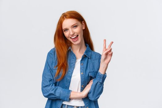 Business, university and people concept. Attractive cheerful redhead woman in denim shirt, send positivity and happiness, showing peace sign and smiling carefree, standing white background