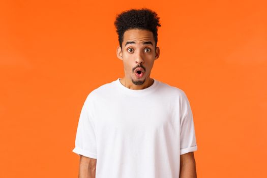 Surprises, amazement concept. Astonished and impressed handsome young college student, african-american guy, folding lips staring amazed, gasping wondered say wow, standing orange background