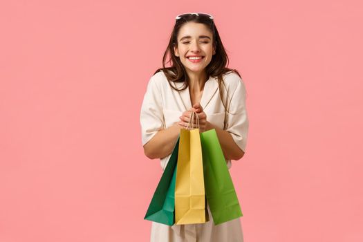 Excitement, consuming and shops concept. Cheerful and amused bride shopping for future wedding, screaming ecstatic, smiling happily holding bags enjoying buying things, standing pink background