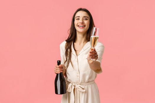 Here drink. Romantic tender young brunette woman opened bottle champagne laughing and smiling giving glass to girlfriend, suggest celebrate special occasion together, pink background