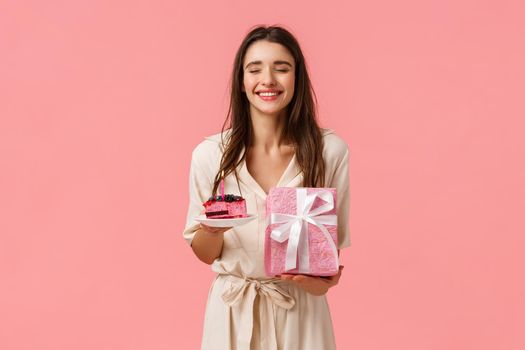 Cheer, happiness and celebration concept. Happy carefree funny young gorgeous woman close eyes dreamy and smiling, receiving congratulations, hold cake and gifts, pink background