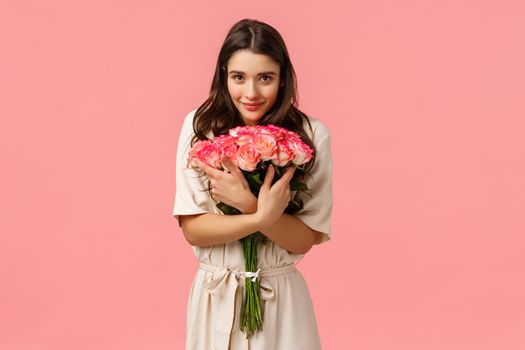 Tenderness, romance and love concept. Attractive brunette female, girlfriend receiving beautiful flowers, hugging bouquet and smiling camera delighted, show affection and happiness, pink background.