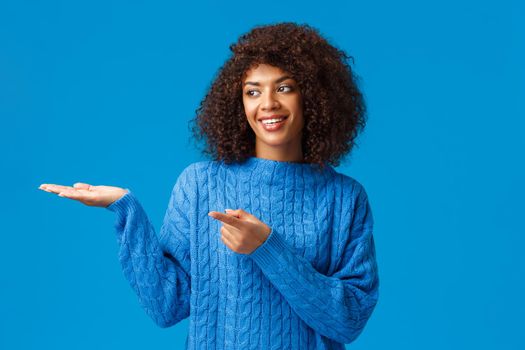 Charismatic lovely smiling african-american female helping family arrange table for holidays gathering, pointing finger left, presenting something on hand, standing blue background joyful