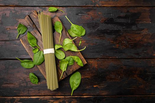 Green colored spaghetti raw dry spinach, on old dark wooden table background, top view flat lay, with copy space for text