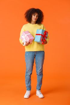 Full-length vertical shot gloomy and displeased picky african-american girlfriend displeased with amount of winter holidays presents, holding two boxed gifts and grimacing dissatisfied