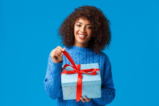 Happiness, holidays and family concept. Happy smiling charming african-american woman with afro haircut, unwrapping gift, pulling knot and smiling cheerful receiving present on new year