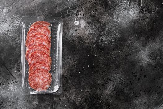 Smoked salami sausages slices in vacuum pack, on black dark stone table background, top view flat lay, with copy space for text