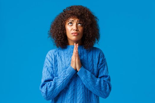 God please help find way. Supplicating faithful and hopeful young african-american woman in need, press hands together and pray looking up sky searching mercy or wayout, standing blue background