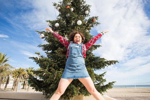 Christmas and holiday concept - Happy jumping woman over Christmas tree background