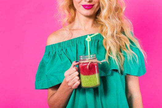 Closeup of woman holding and drinking tasty green smoothie milkshake on pink background