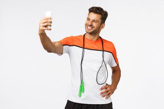 Healthy lifestyle, sport and people concept. Handsome happy smiling muscular man promote active leisure, taking selfie smartphone, grinning proud during endurance workout, gym training with jump rope