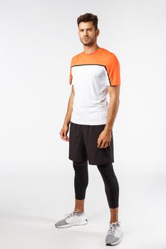 Vertical studio shot male football player in activewear, sneakers standing determined, ready score goal, squinting frowning self-assured, prepare for workout, endurance and sport concept