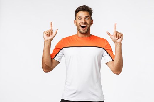 Astonished, fascinated masculine bearded man, masculine sportsman gasping amused, open mouth amazed, see something stunning, smiling happy, pointing up, advertise great productm white background