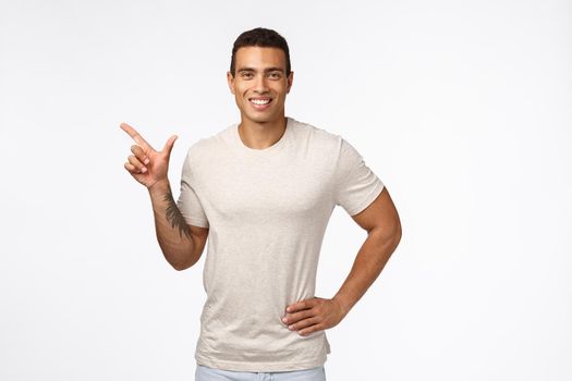 Sports, healthy people and movember concept. Handsome smiling hispanic guy in casual t-shirt, hold hand on waist relaxed, pointing left and grinning satisfied, recommend promo, advertise new product