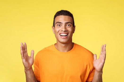 Attractive, excited caucasian man in t-shirt showing box or something big, spread hands near chest to form large object, explain something, discuss vast sales, having dialogue, yellow background