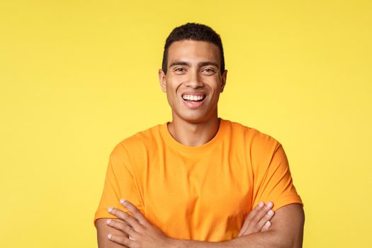 Joyful smiling handsome masculine man in t-shirt, cross arms chest confident, laughing as having carefree, relaxing conversation during party, standing yellow background upbeat, self-assured