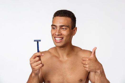 Close up of a happy naked african man holding razor isolated over gray background.