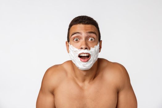 Close up of a happy naked african man with face in shaving foam isolated over gray background