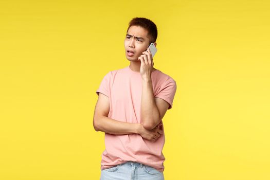 Technology, communication and lifestyle concept. Portrait of frustrated, disappointed asian guy talking on phone, discuss problem on phone, use smartphone and frowning complicated
