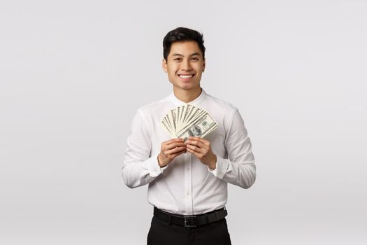 Look at that cash. Handsome happy and rich young asian guy ready spend paycheck on shopping, holding money and smiling, winning sport bid, achieve success corporate ladder, white background