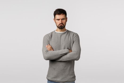 Offended grumpy cute bearded boyfriend feeling let down and displeased, standing insulted, partner hurt his feelings, cross arms chest defensive, make sad expression, standing angry white background