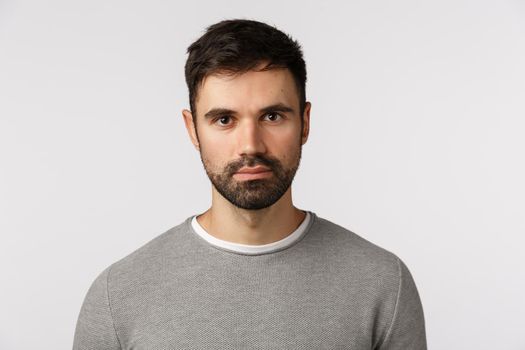 Close-up shot serious and determined handsome, adult masculine bearded man in grey sweater, looking with casual expression camera, standing still, awaiting important news, white background