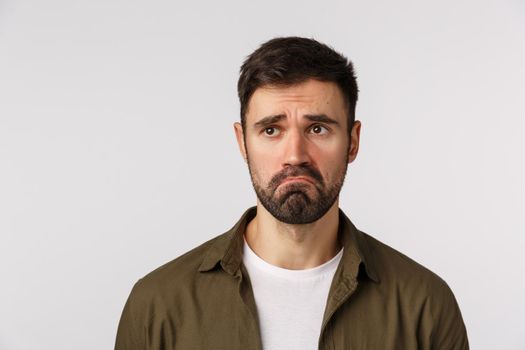 Miserable cute and insecure sad, lonely adult guy making pitiful sorry smile, frowning look with compassion and sadness left, standing jealous or express regret, posing white background in coat