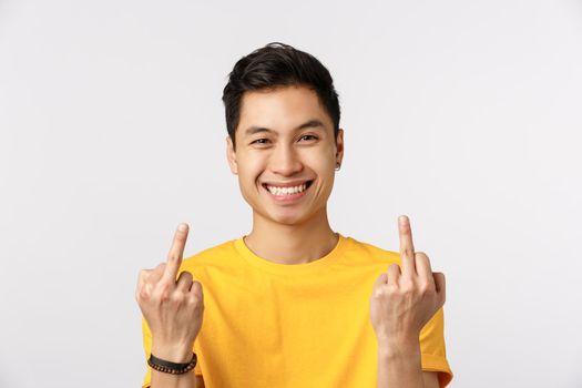 Go fuck yourself. Unbothered and careless young millennial chinese man showing middle fingers and smiling, dont care at all, acting provocative and rebellious, standing white background