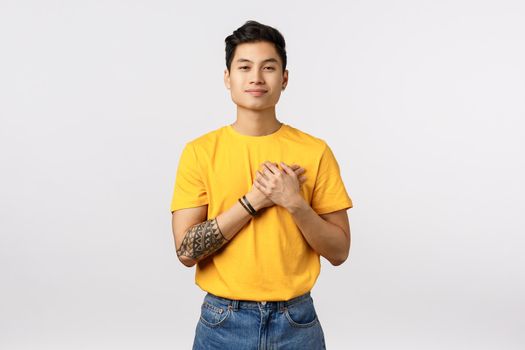 Touched, dreamy handsome young asian boyfriend with tattoos, wear yellow t-shirt, cherish tender moment with girlfriend valentines day, smiling touched, contemplate something beautiful, breathtaking