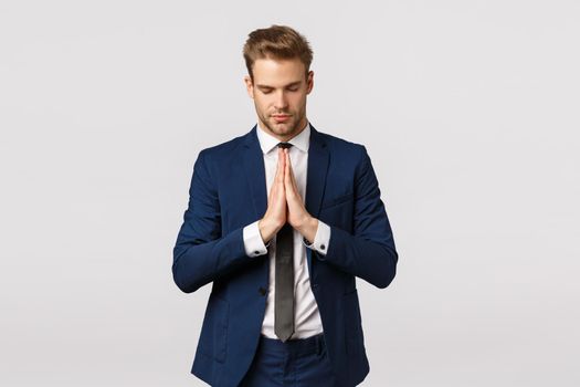 Concentrating mind and soul. Peaceful and calm successful blond bearded businessman, young male entrepreneur in suit, clasp hands together in pay, supplicating, meditating with closed eyes