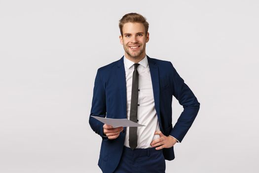 Business, entrepreneur and economy concept. Handsome young blond businessman with bristle, hold hand on waist in confident, carefree pose, holding papers, discuss documents, corporate plan
