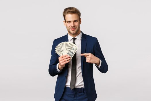 Check this out, how success looks like. Handsome businessman with cash in hands, pointing money and smiling confident, bragging, discuss how manage business, starting own company