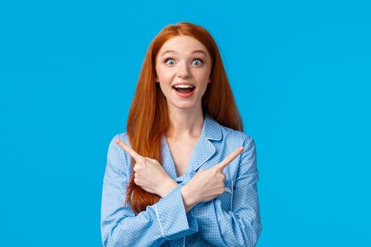 Surprised and amused beautiful redhead teenage girl, female college student playing with roommates in nightwear, pointing left and right, sideways with crossed hands amazed, see lots choices