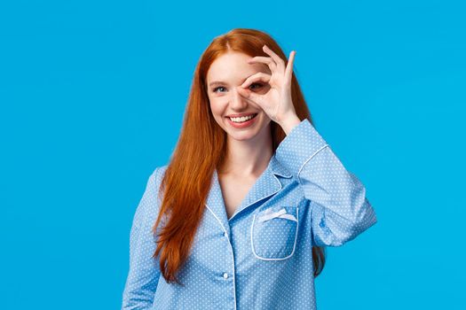 Excellent choice right here. Charismatic satisfied redhead female in nightwear showing okay gesture, promote beauty products, dont worry about menstrual period, standing blue background
