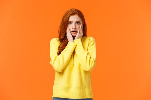 Concerned and anxious redhead girl forgot take chicken out freezer before mom came home, grab face, gasping scared and troubled, dont know what do, standing tensed and afraid, orange background