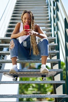 Black woman, with coloured braids, watching something funny on her smartphone.