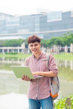 Attractive male asian student is using laptop in campus