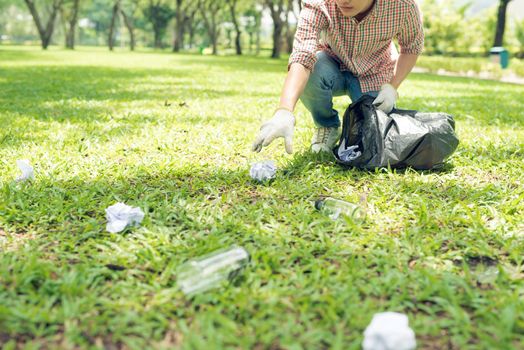 Young man crouching to waste and picking it up in bin bag