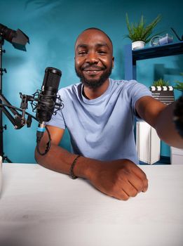 Portrait of smiling famous influencer taking wide angle selfie in podcast recording studio