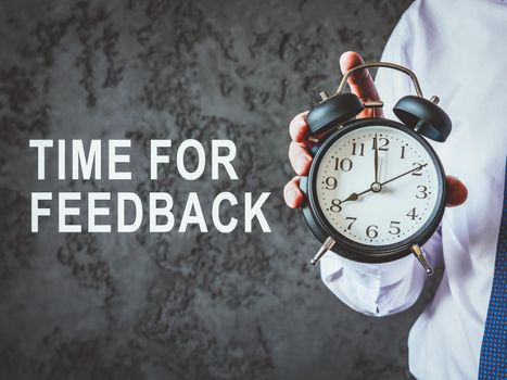 Time for feedback. Man shows alarm clock.