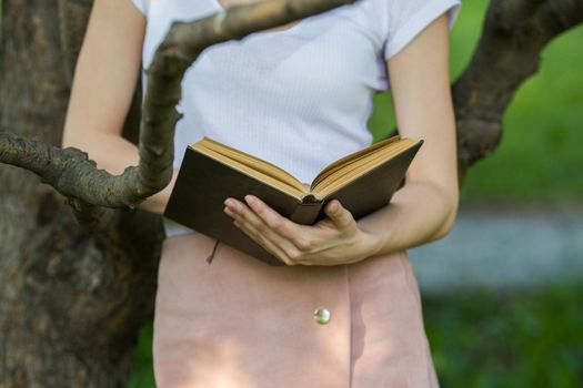 Young woman holding a book in hands leaning on a tree branch