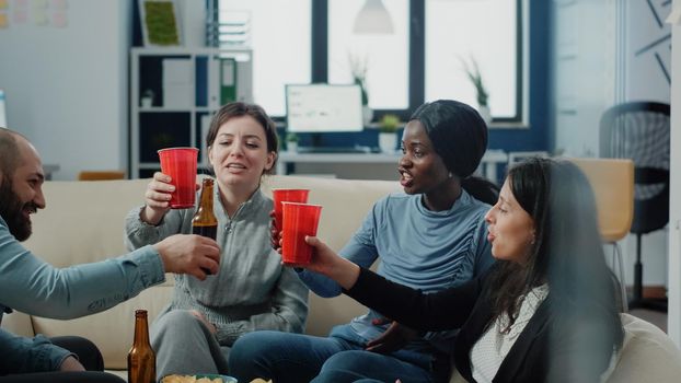 Cheerful coworkers cheers with cups and bottles of beer