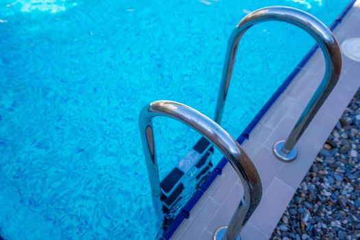 Background of blue transparent water in the swimming pool on the territory of the hotel. Descent to the pool with handrails. Rest and relaxation concept. Active rest by the sea