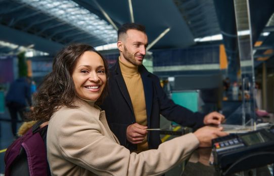 Beautiful middle aged ethnic couple - woman of Middle Eastern descent and handsome Caucasian man holding out passports while going through passport and customs control at international airport